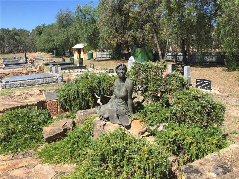 Beautiful sculpture of a young woman, gravesites, headstones, grass, sunny day..