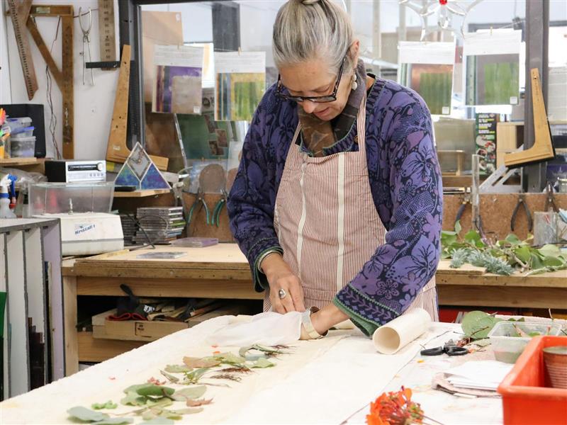 A woman rolling up a silk scarf with botancial matter laid out on it