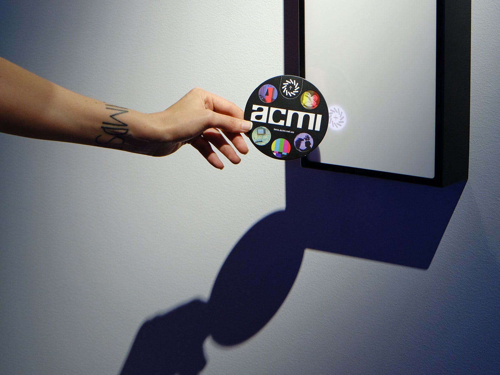 A hand holds a circular disc up to a white box