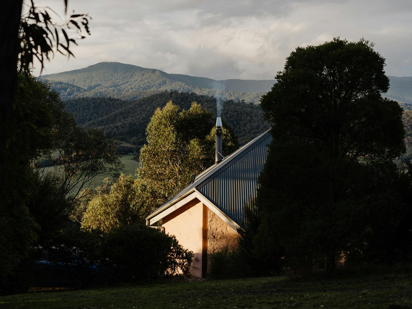 A hidden mudbrick cabin with smoke coming out of the chimney with mountains in the background