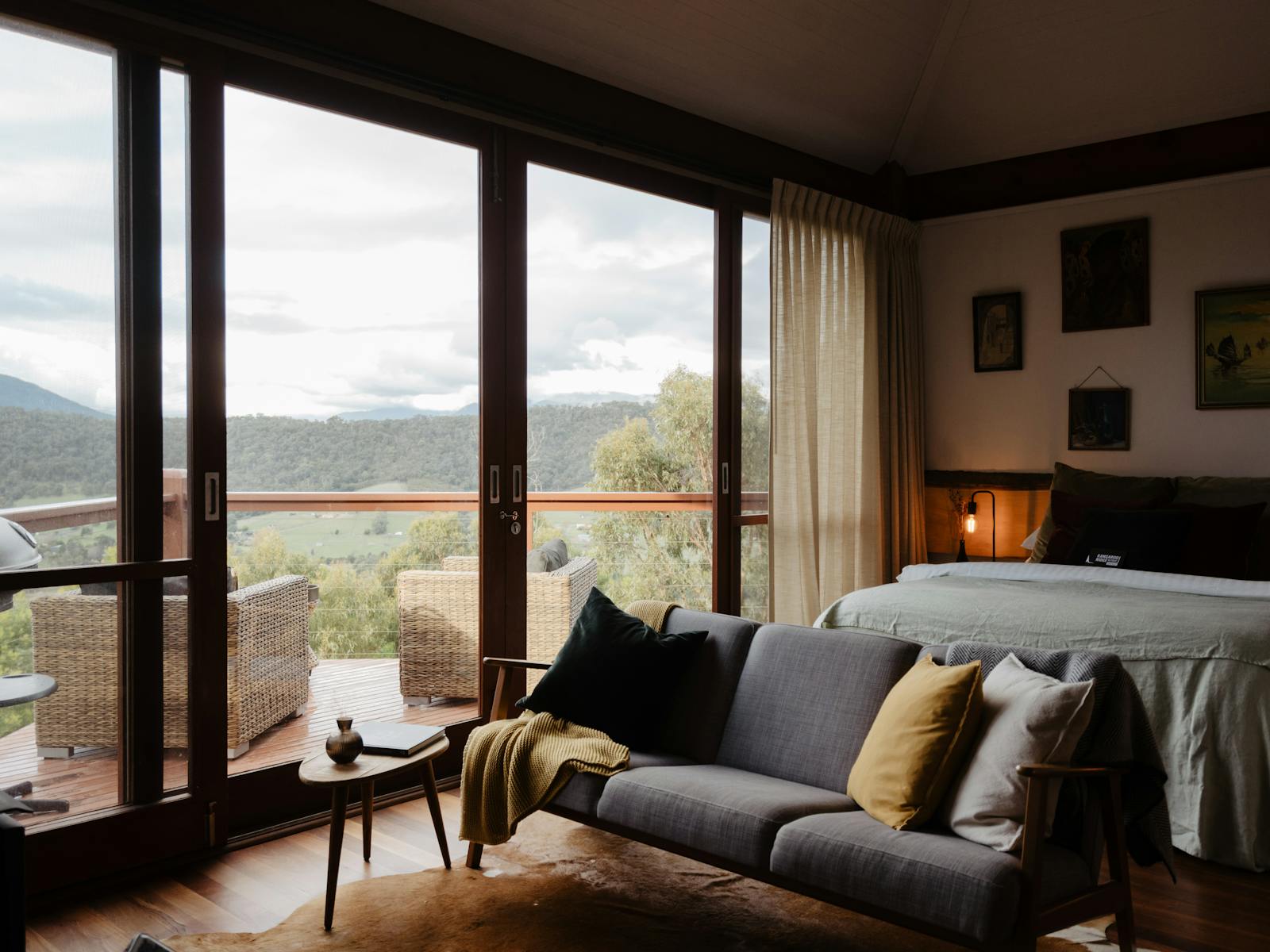 Interier of the cabin showing a bed and couch with mountain views from the floor to ceiling windows.
