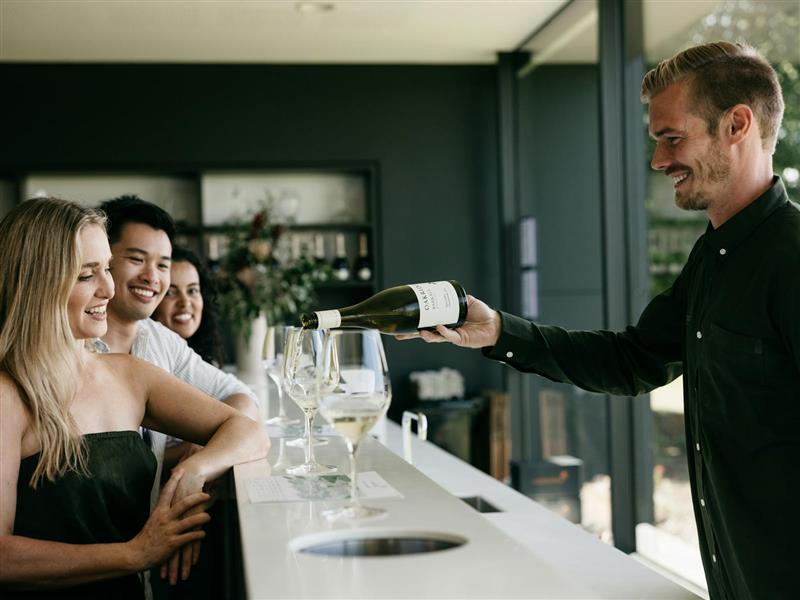 3 guests sit at the tasting bar while a smiling staff member pours Oakridge Chardonnay