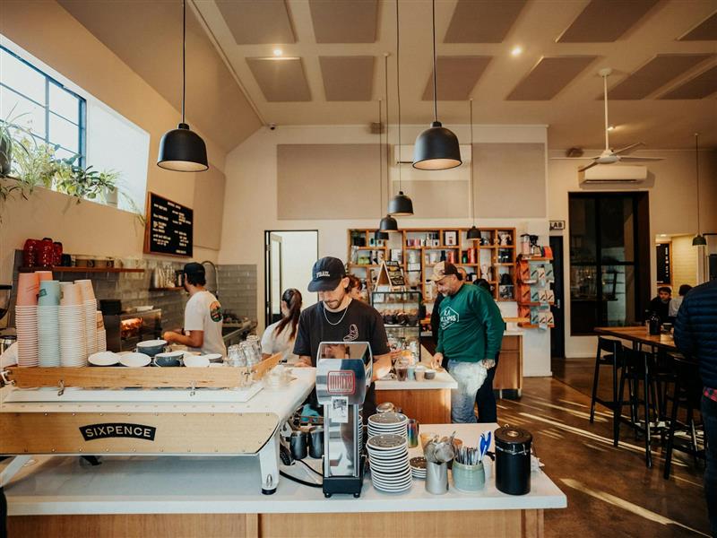 Man making coffee in black t-shirt and black cap at white branded coffee machine in open room