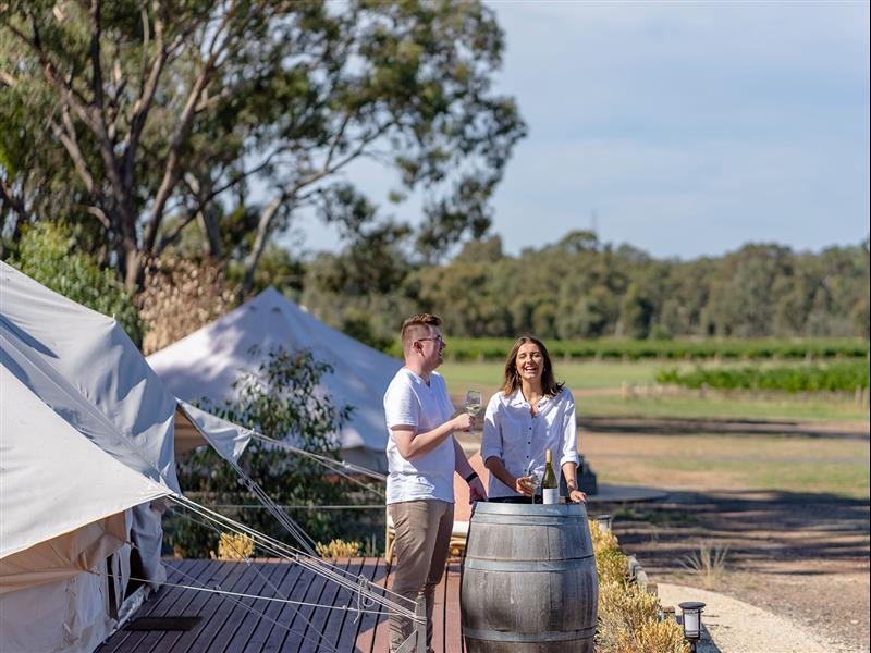 A laughing couple share a bottle of wine outside a glamping tent at Balgownie Estate, Bendigo.